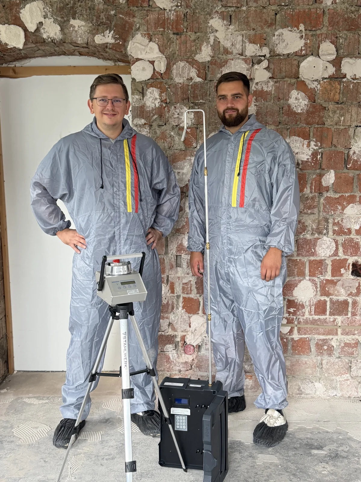 Dr. Stefan Peischard (links) und Markus Knaub (rechts) im Schutzanzug mit Luftkeimsammler und Kofferpumpe in einem entkernten Altbau